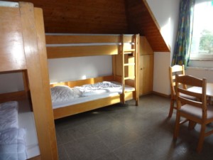 Ein Schlafzimmer mit Etagenbetten, Sitzgruppe und Kleiderschrank im Gruppenhaus Freizeitheim Settrup für Kinder und Jugendfreizeiten in Deutschland.