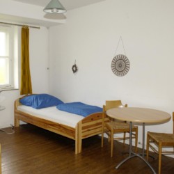 Ein Schlafzimmer mit Holzbetten, Sitzgruppe und Kleiderschrank im niedersächsischen Freizeitheim Settrup für Kinder und Jugendfreizeiten in Deutschland.
