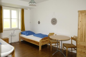 Ein Schlafzimmer mit Holzbetten, Sitzgruppe und Kleiderschrank im niedersächsischen Freizeitheim Settrup für Kinder und Jugendfreizeiten in Deutschland.