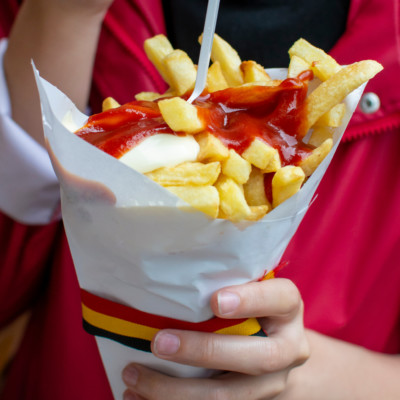Eating of Belgian fried potatos chips with ketchup and mayonnaise, street fast food, unhealthy food
